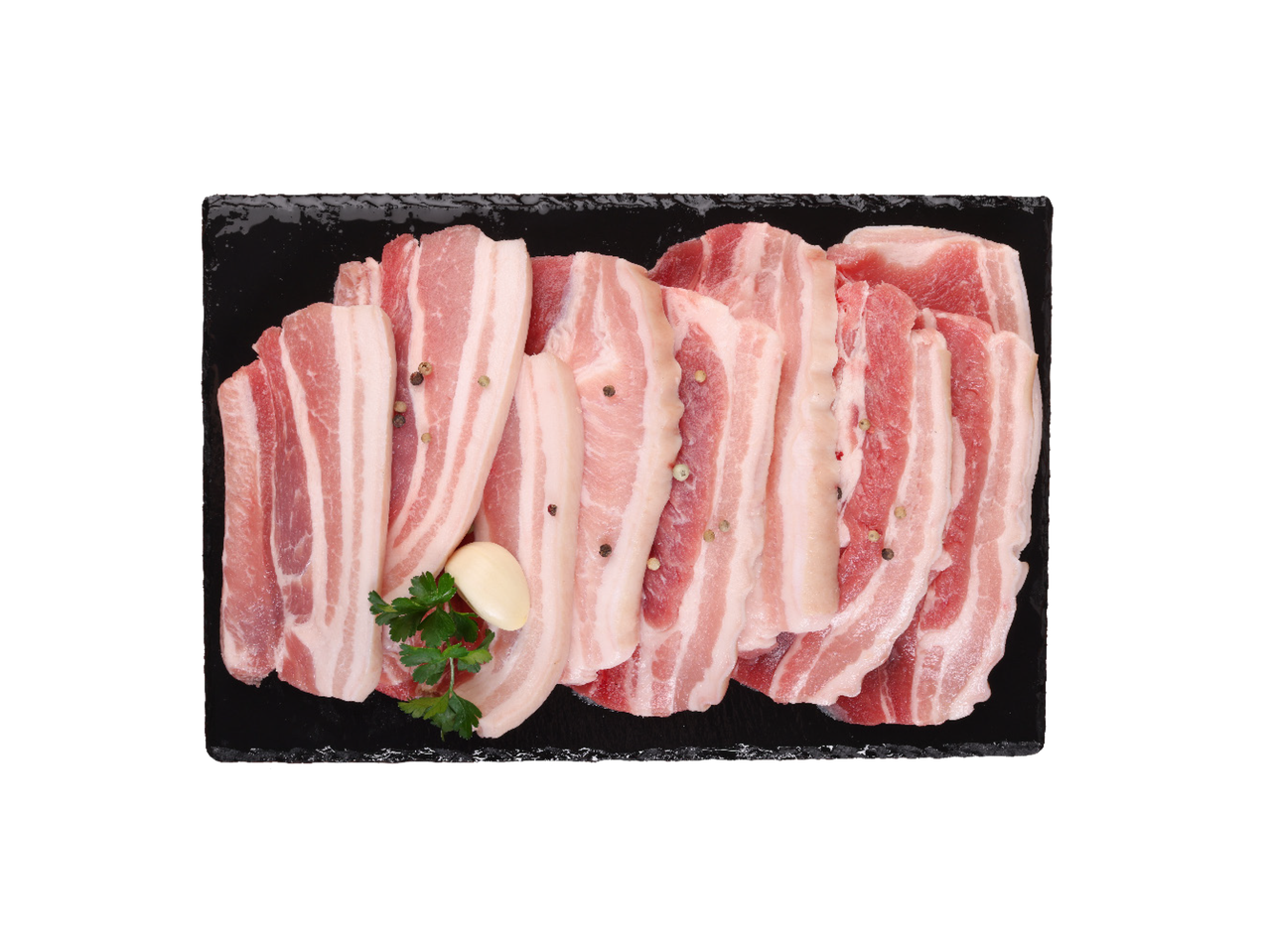 Sirova svinjska slanina isečena na trake sa belim lukom i peršunom na crnoj ploči.