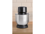 Robô de cozinha com tampa preta e taça de aço inoxidável sobre uma superfície de madeira.
