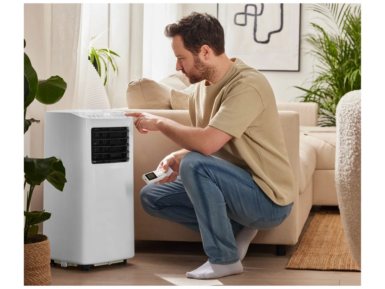 Un homme règle un climatiseur portable avec sa télécommande.