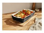 Roasted chicken and vegetables in a black baking dish on a wooden board.
