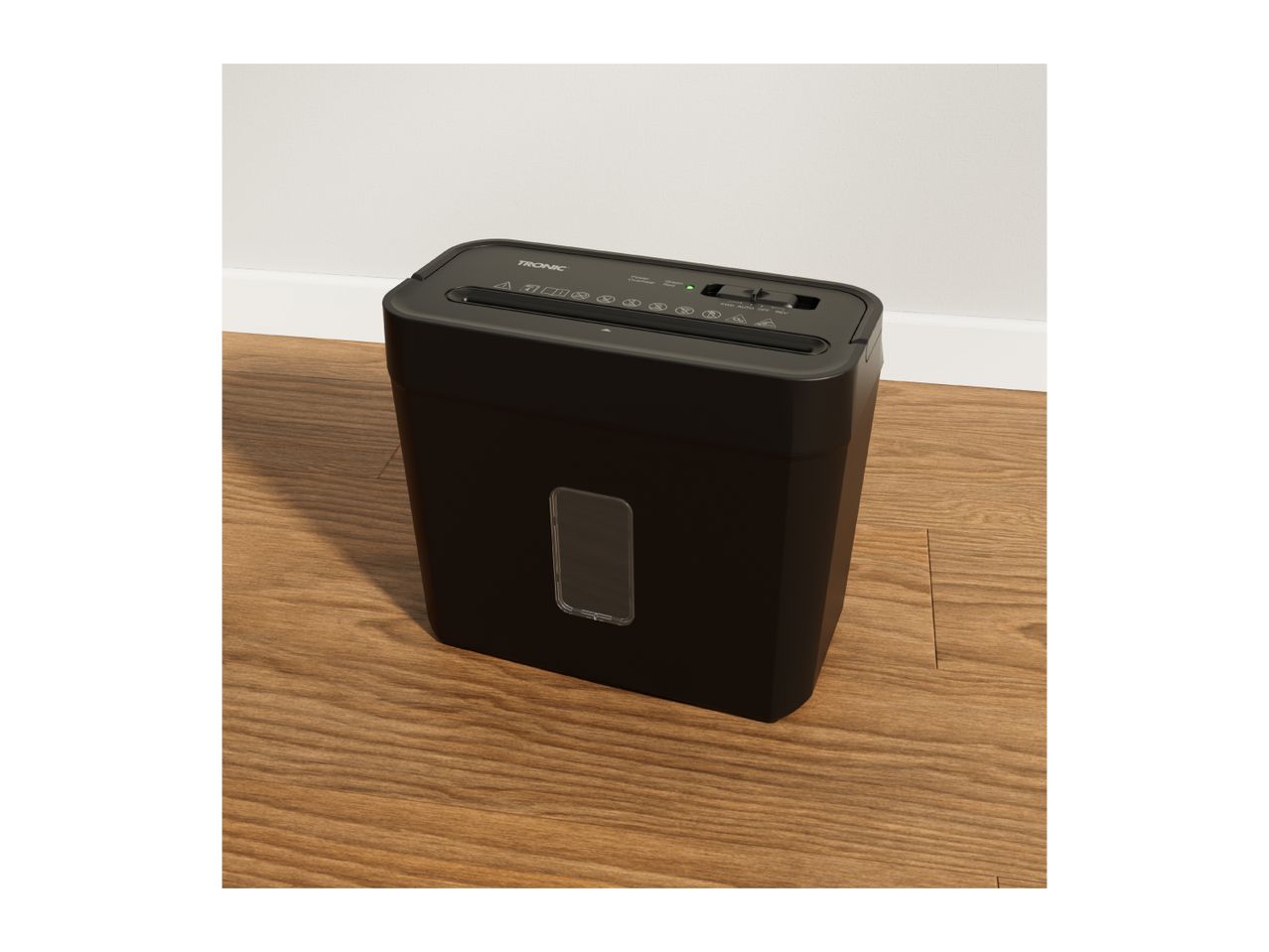 Black paper shredder with a clear window on a wooden floor next to a white wall.