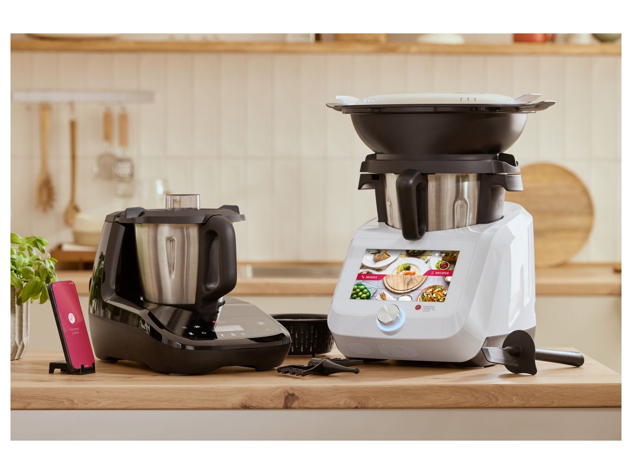 Two Monsieur Cuisine food processors, one black and one white, on a kitchen counter.