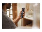 A man holding a black trimmer with a green blade in a bathroom.