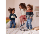 Three happy children jumping on a bed with a dinosaur-patterned duvet.