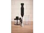 Black immersion blender with a chopper attachment and a measuring cup on a wooden surface.