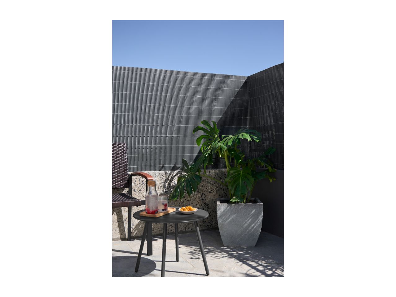 Outdoor patio with a small black table, drinks, snacks, and a large potted plant.