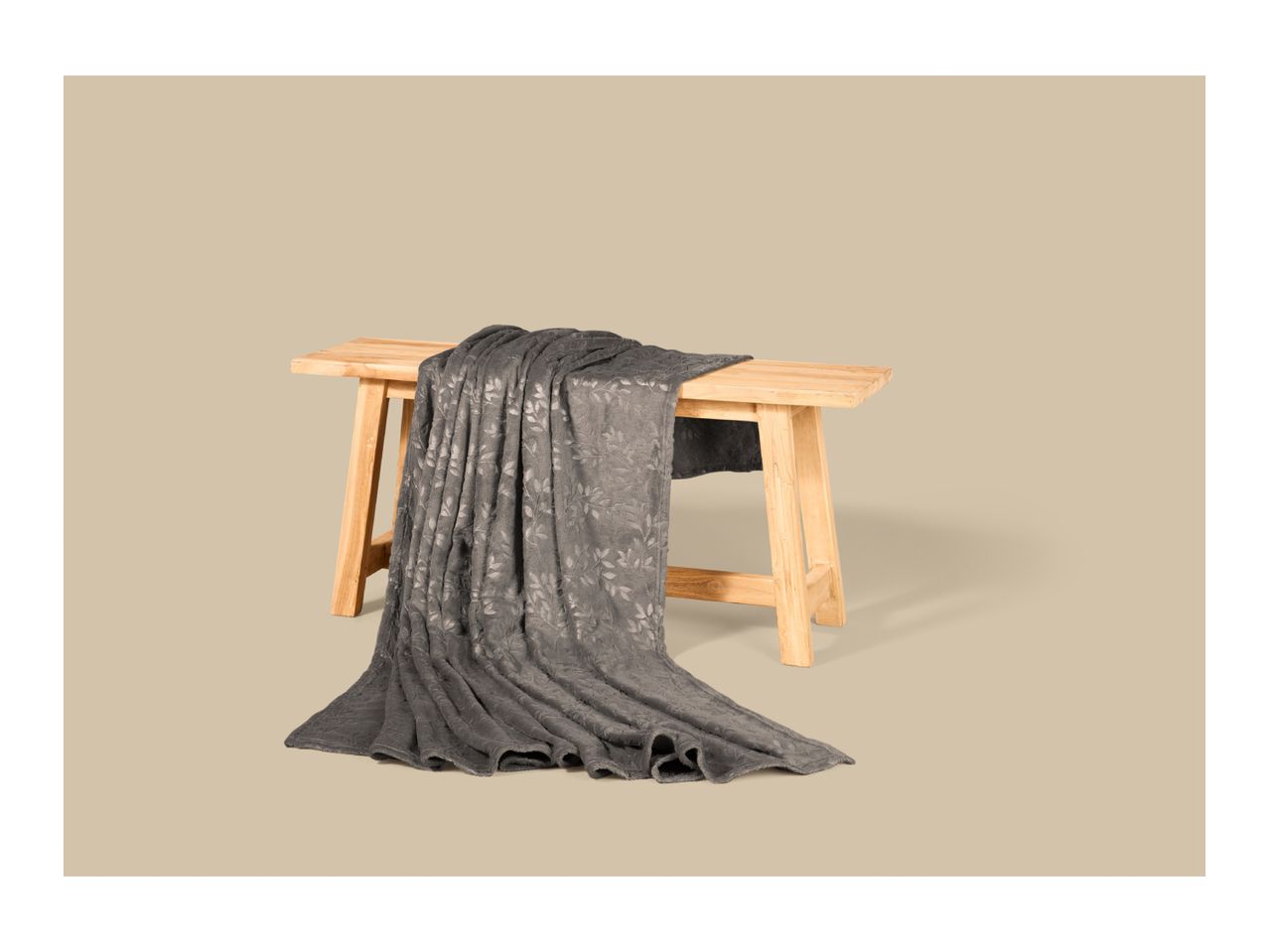 A grey patterned blanket draped over a light wooden bench.