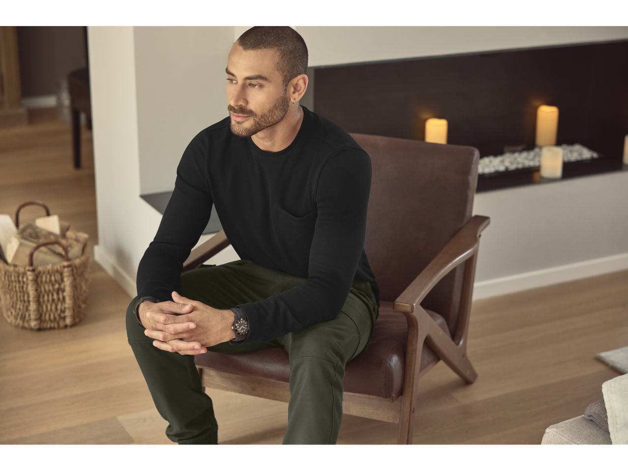 Man in black long-sleeve shirt and green joggers sitting in a chair.