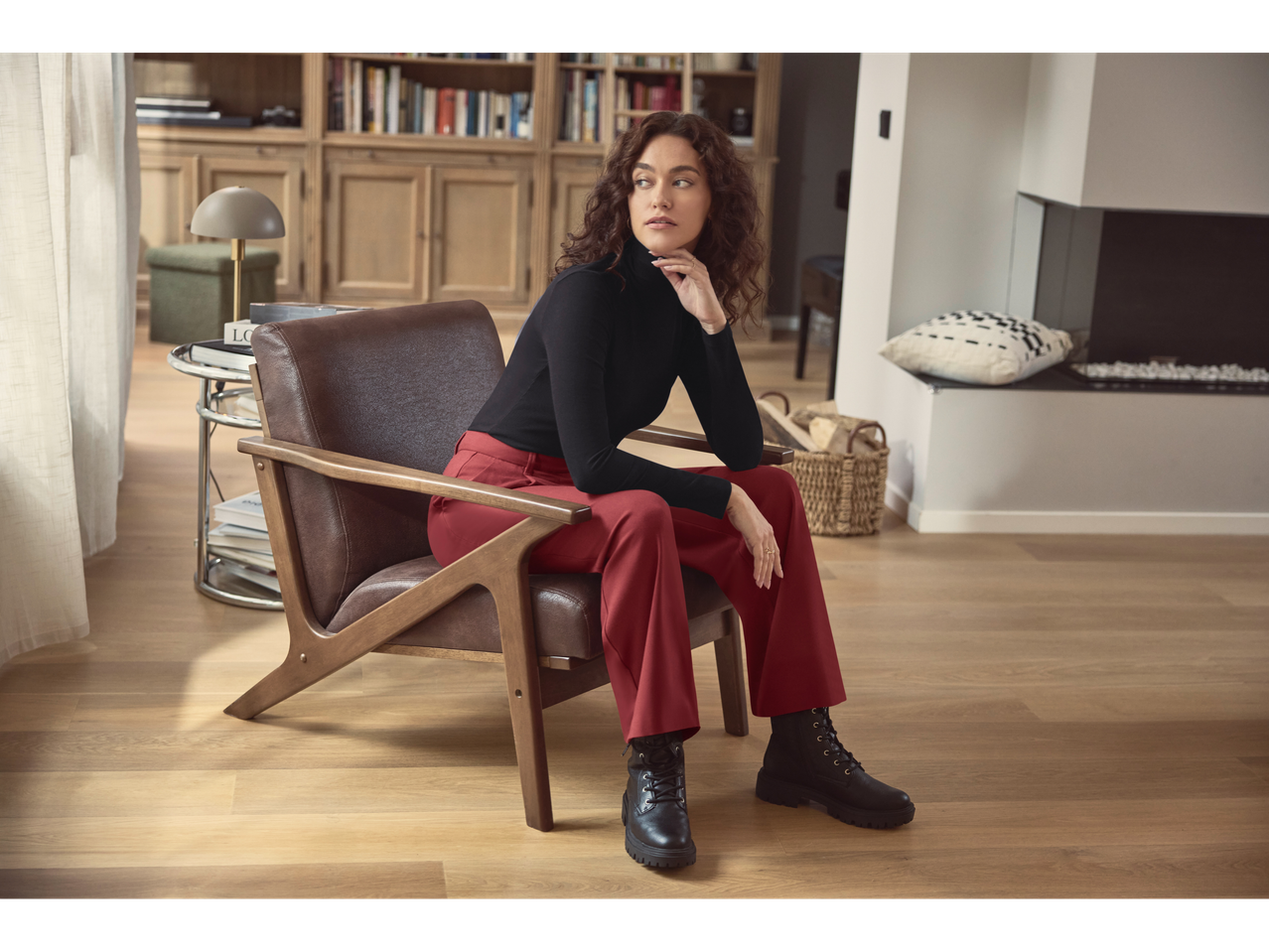 A woman in esmara® wide leg trousers and a black turtleneck sits in a living room.