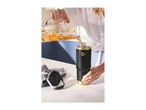A person pouring iced tea with fruit slices from a pitcher into a black and gold insulated tumbler.
