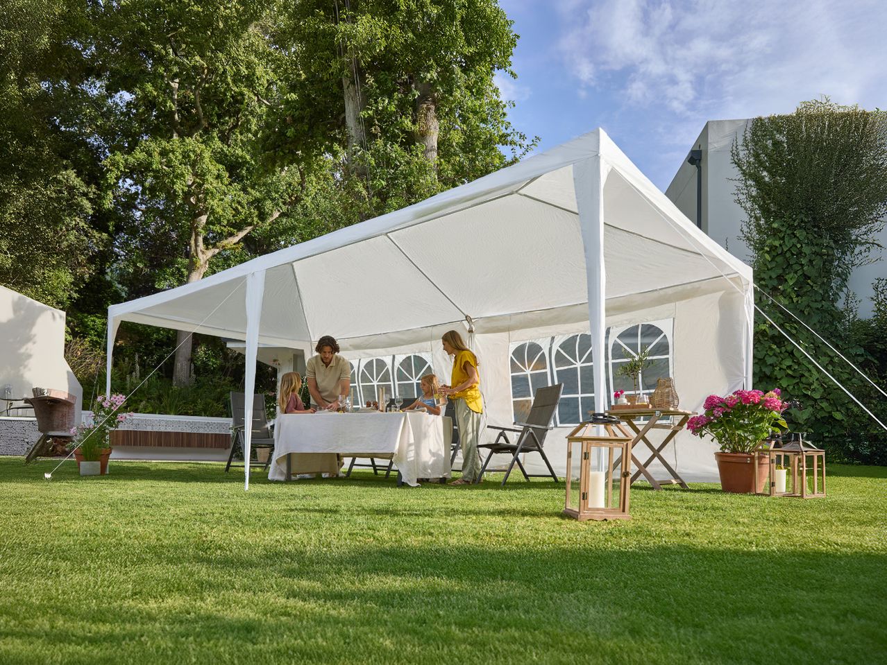 Family enjoying a meal under a white party tent in a garden with green grass.