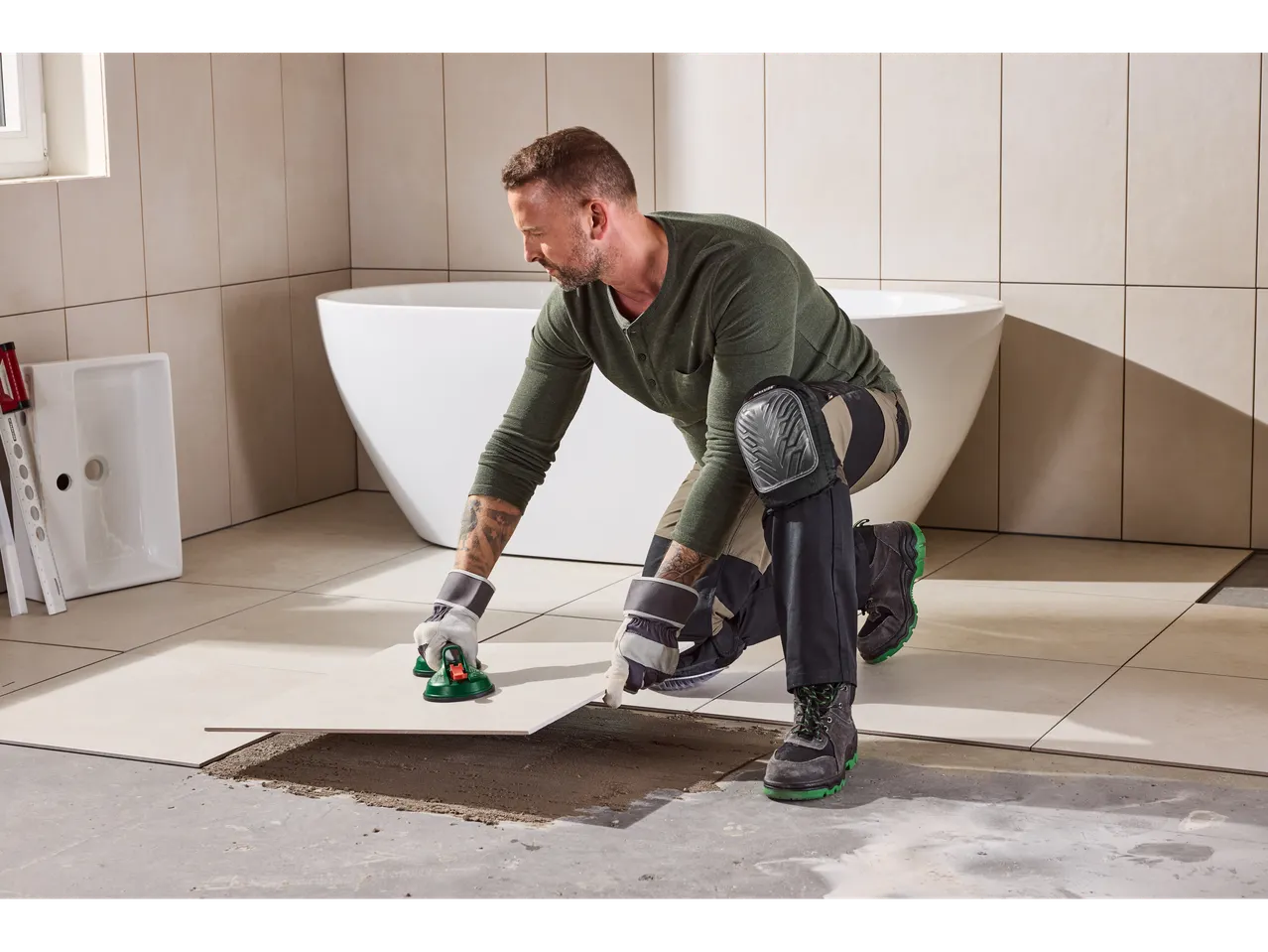 Muškarac postavlja kupaonske podne pločice s vakuumskom čašom i štitnicima za koljena.