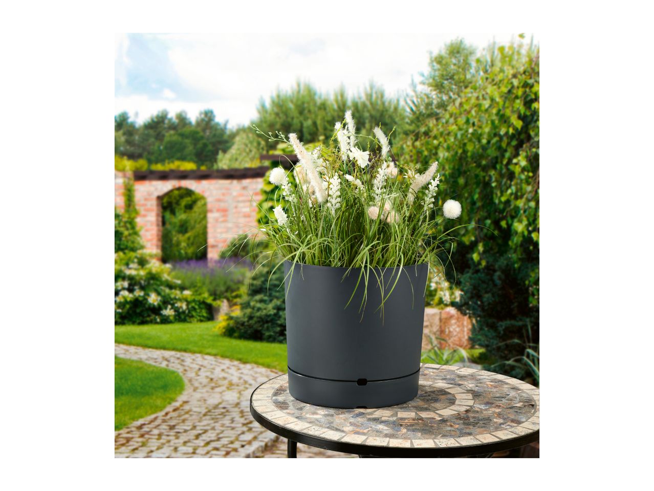 Dark grey planter with white and green plants on a mosaic table in a garden.