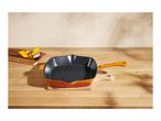 Orange cast iron grill pan on a wooden table with vegetables.