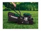 A person operating a green and black petrol lawnmower with a grass collection bag on a lawn.