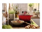 A red Dutch oven on a stovetop with a bowl of food and kitchen utensils.