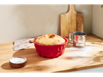 A baked cake in a red SILVERCREST® silicone mold on a wooden counter with flour.
