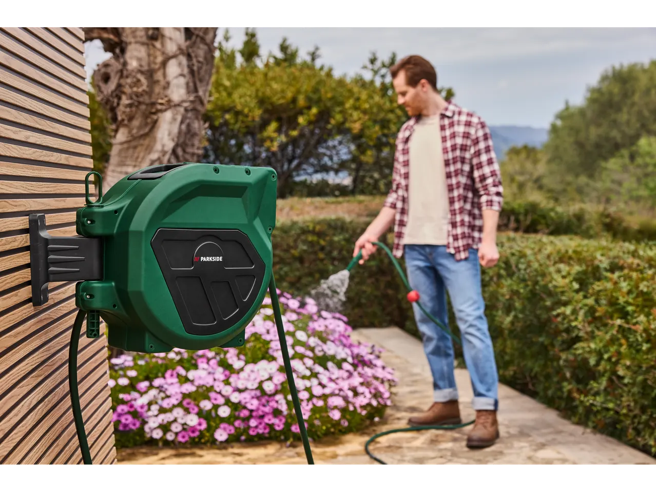 A man waters his flowers with a hose on a Parkside reel.