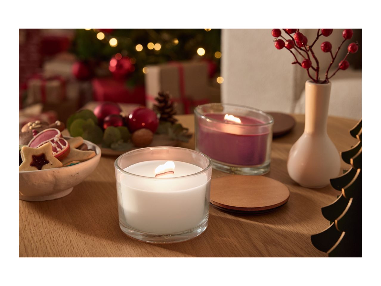 Christmas table setting with two lit candles, cookies, and festive decorations.