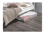 An under-bed storage bag with a clear window, filled with textiles, sits on a wooden floor next to a bed.