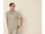 Homem sorridente de óculos, polo verde e calções bege.