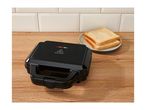Black sandwich maker on a wooden surface with two slices of bread on a plate.