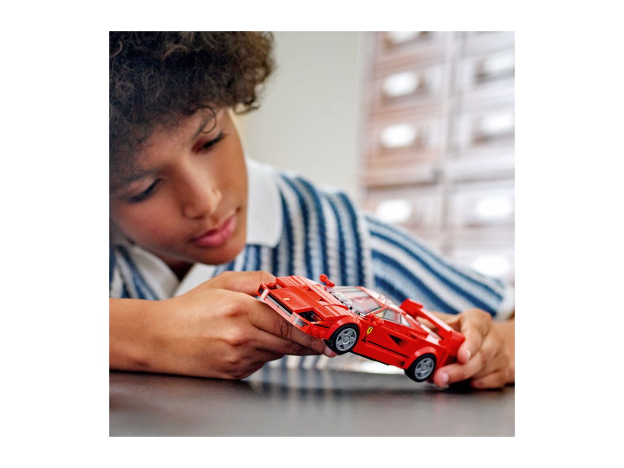 Child playing with a red toy car on a table.