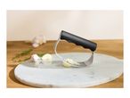 Garlic press with crushed garlic, garlic cloves, and thyme on a marble board.