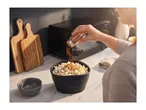 Person seasoning popcorn in a black bowl on a kitchen counter with cutting boards.