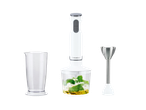 White hand blender with a measuring cup and a chopper bowl containing pesto ingredients.