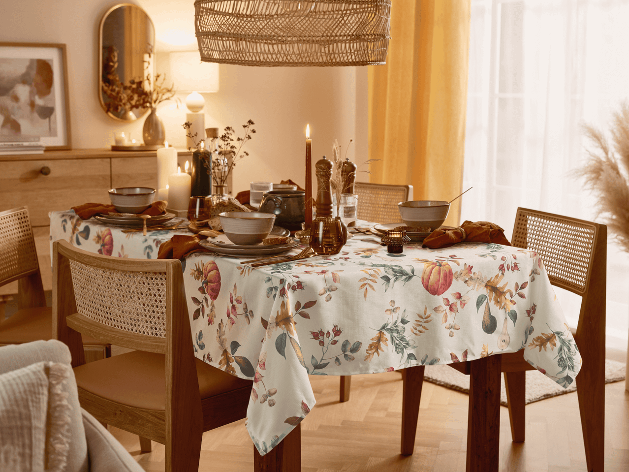 Esstisch mit herbstlicher Tischdecke, Geschirr und Kerzen in einem warm beleuchteten Raum.