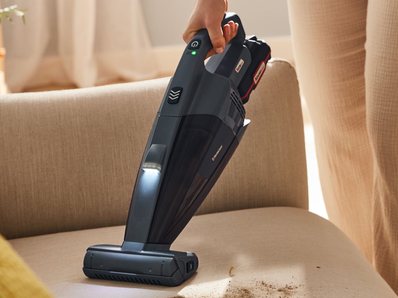 A person uses a handheld vacuum cleaner to clean a couch.