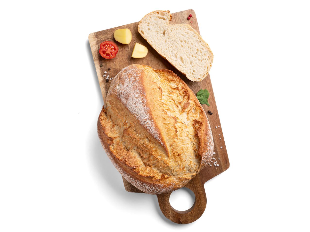 Egy fa vágódeszkán egy egész és egy fél kenyér, paradicsommal és burgonyával.