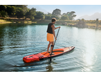 Homem a praticar paddleboard num lago rodeado por árvores e montanhas.