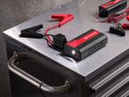Jump starter with clamps and a battery charger on a metal workbench.
