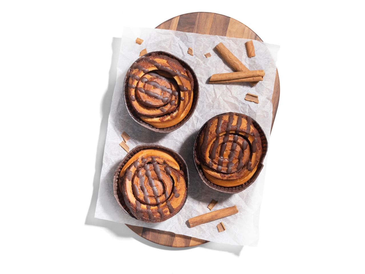 Három fahéjas csiga csokoládéval egy fa deszkán.