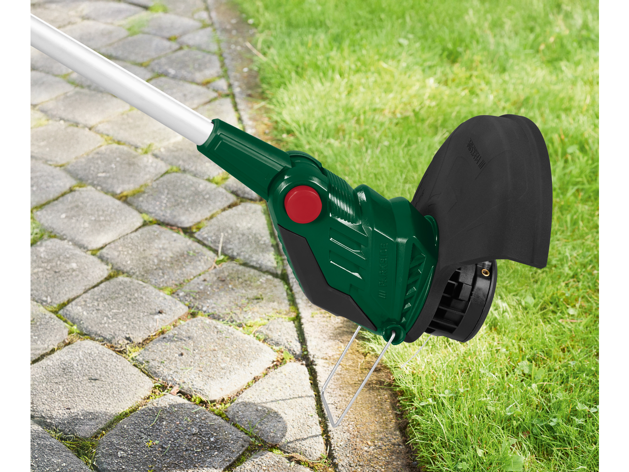 Trimmer verde de gazon cu apărătoare neagră, lângă o alee pavată și iarbă.