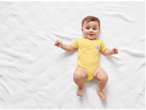 Bebeluș pe o pătură albă îmbrăcat într-un body galben.