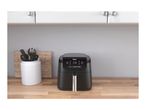 Black air fryer on a wooden kitchen counter next to a utensil holder.