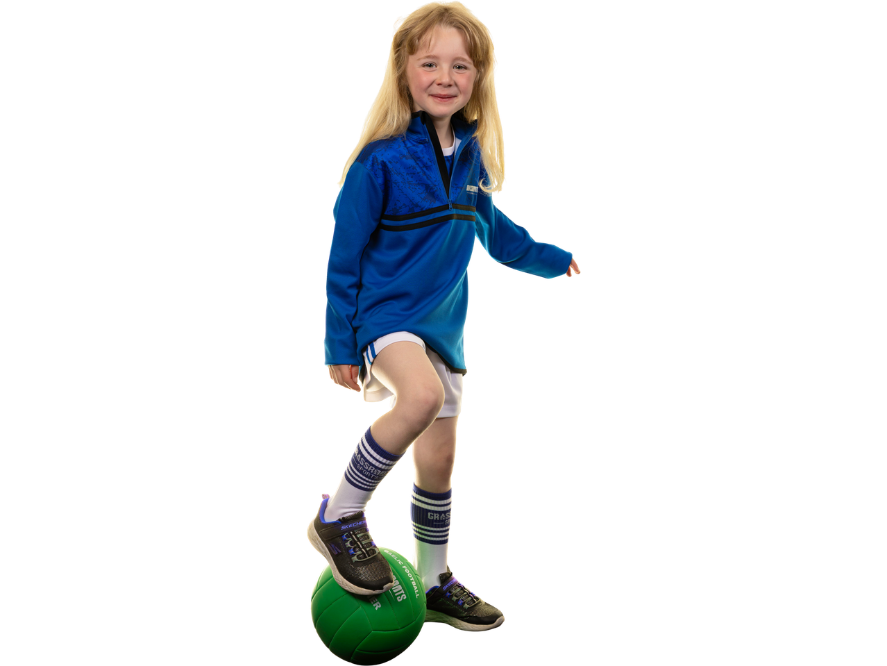 Young girl in a blue training jersey and white shorts, with a green Gaelic football.