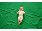 Happy baby in a beige bodysuit and leggings on a green waffle blanket.