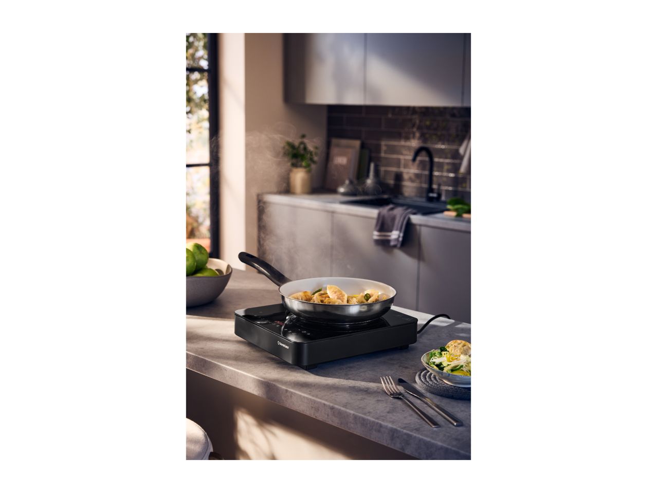 Induction hob with a frying pan cooking dumplings, next to a bowl of salad in a modern kitchen.