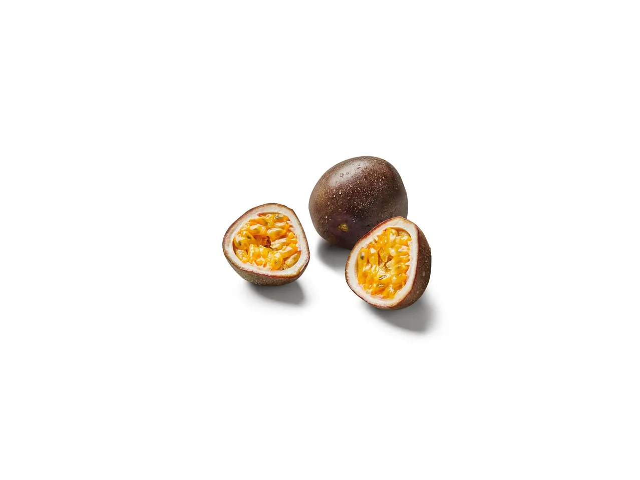 Zwei halbierte Passionsfrüchte und eine ganze Passionsfrucht liegen auf weißem Hintergrund.