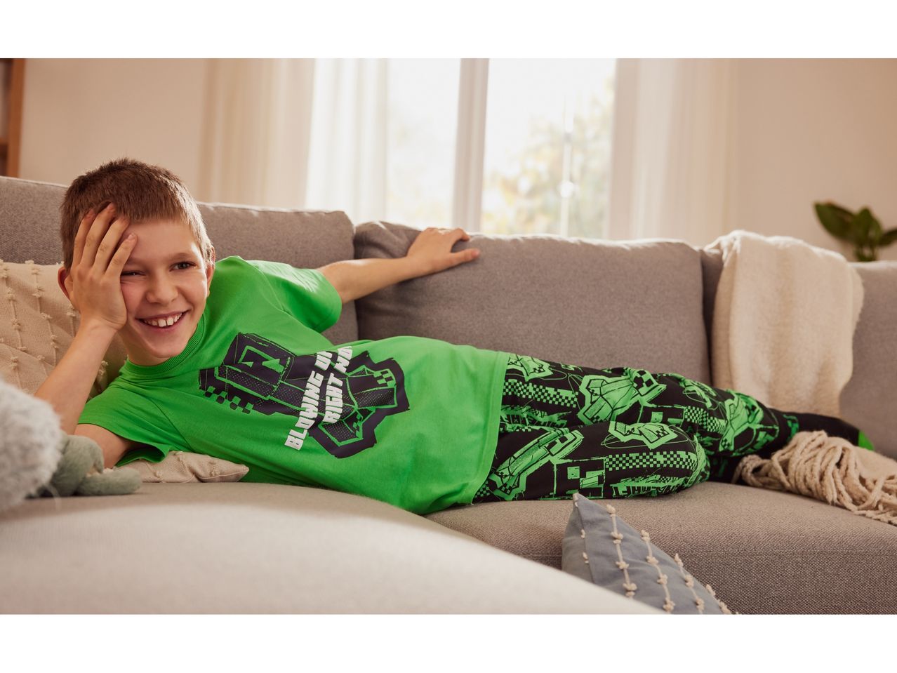 Boy relaxing on a couch wearing a green monster-themed pajama set.