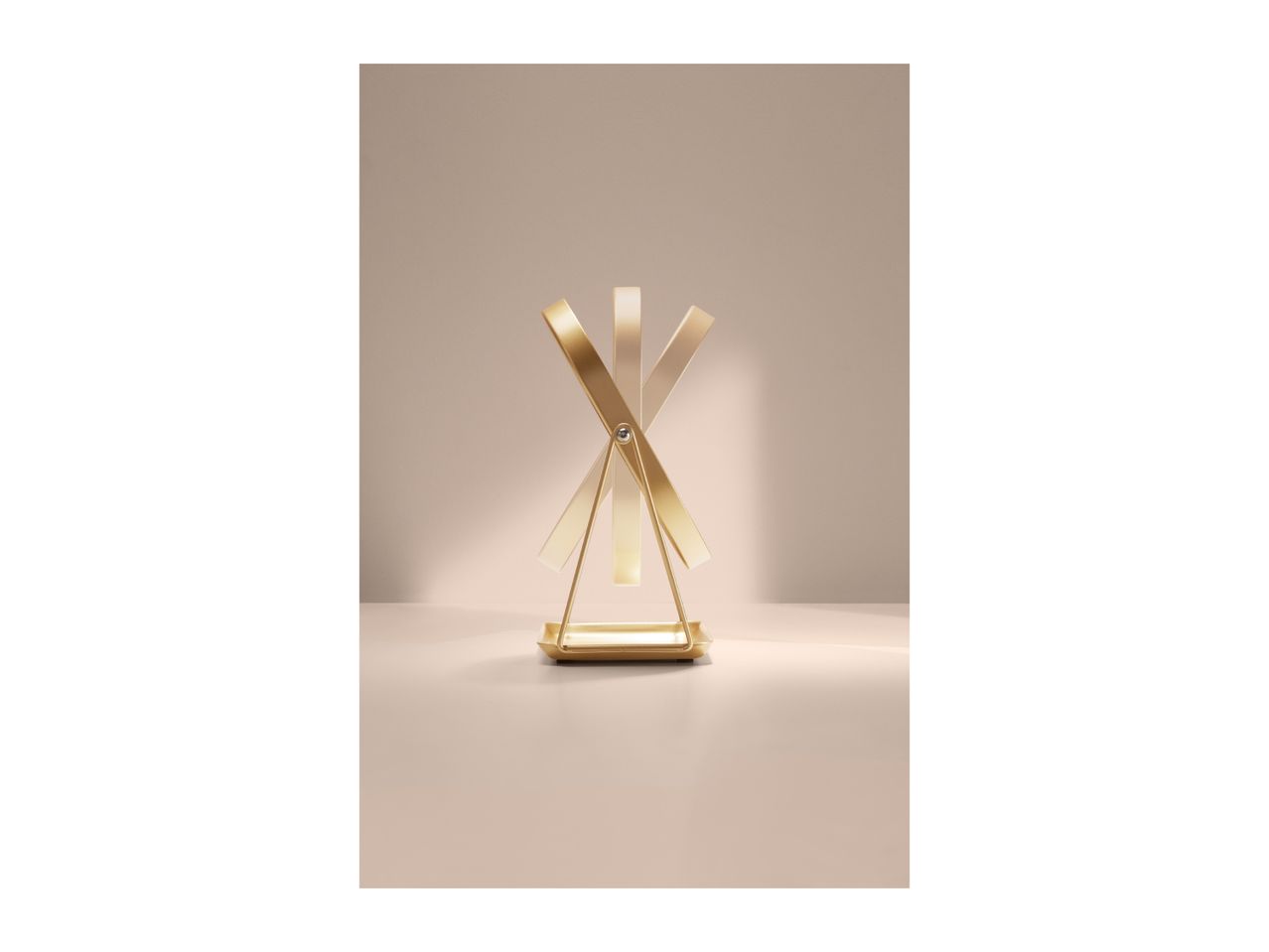 Gold-colored rotating mirror with a rectangular base on a light beige surface.