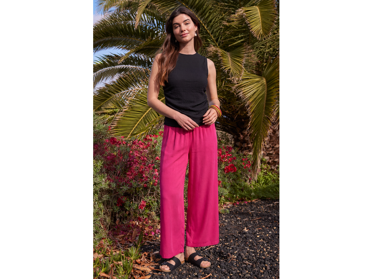 Femeie în top negru ESMARA și pantaloni largi fucsia, sandale negre, într-o grădină.