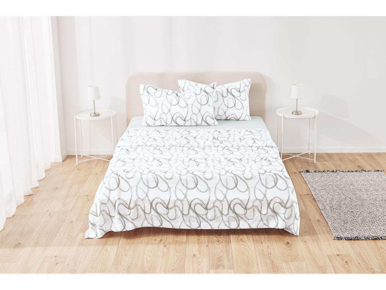 A bed with white sheets with a gray pattern, two nightstands with lamps, and a rug in a bedroom.