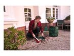 Man sweeping leaves into a green garden bag with a broom and dustpan.