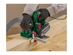 Person using an electric planer on a wooden plank, with a dust extraction hose attached.