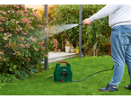 Homem regando um arbusto de flores rosa com uma mangueira de jardim e um enrolador.